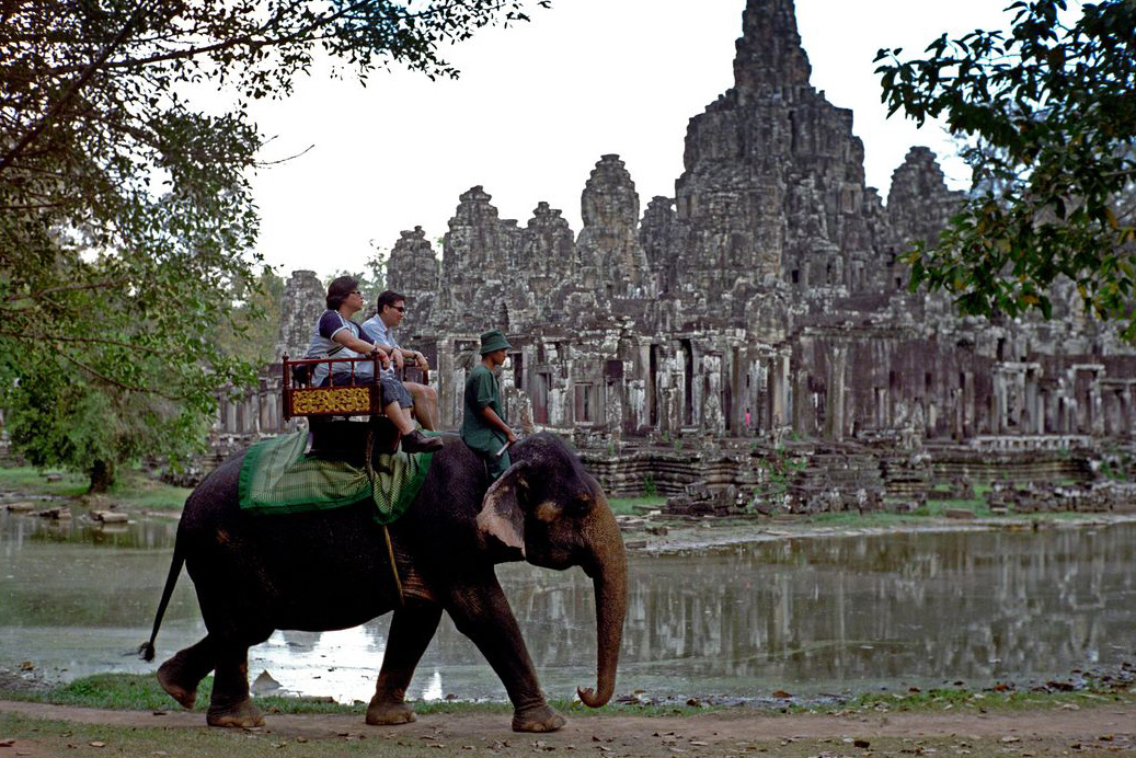 Cambodia. Angkor. Tourists ride an elephant by the lake in front of the Bayon temple.