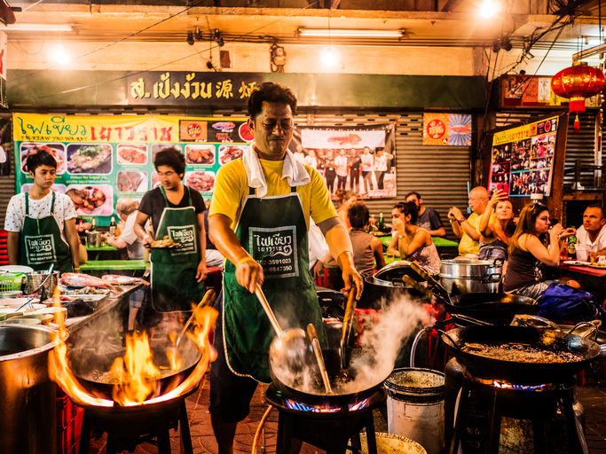 Bangkok, Thailand - February 26, 2016: A cook is preparing food in a restaurants with chairs and tables on the street at Chinatown Bangkok. This area is very popular because the diverse food stands that appear at night time.